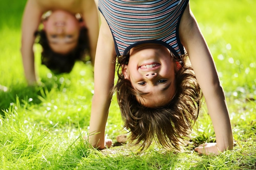 Portraits of happy kids playing upside down outdoors in summer park