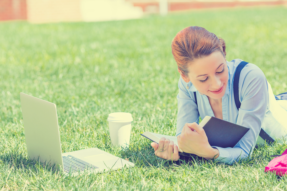 Student studying in park. Joyful happy young girl student sitting reading book outside on university campus or park. Education concept. Positive face expression Student studying in park. Joyful happy young girl student sitting reading book outside on university campus or park. Education concept. Positive face expression