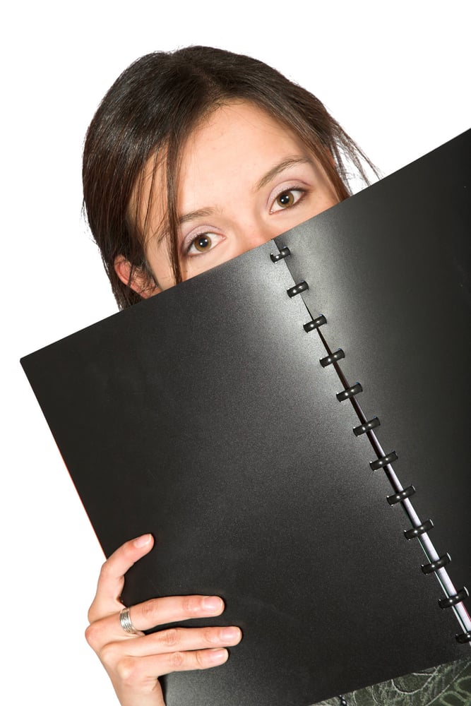 beautiful teen peeping over notebook over white